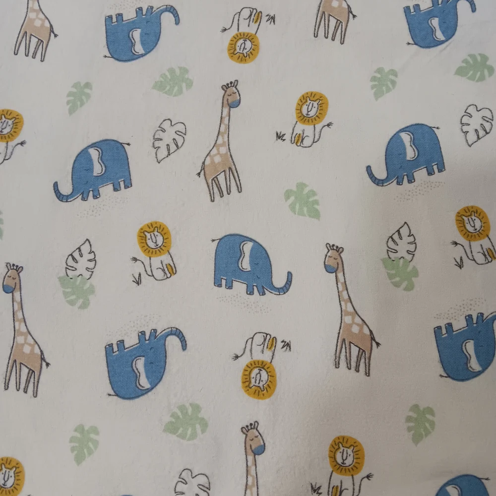 Franela suave para bebé con estampado de jirafas, elefantes y leones sobre fondo beige.