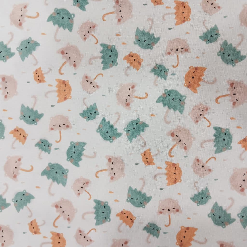 Tela de algodón con estampado de paraguas con caritas adorables en tonos pastel: verde menta, rosa y mostaza, sobre fondo blanco. Estilo suave, infantil y alegre.