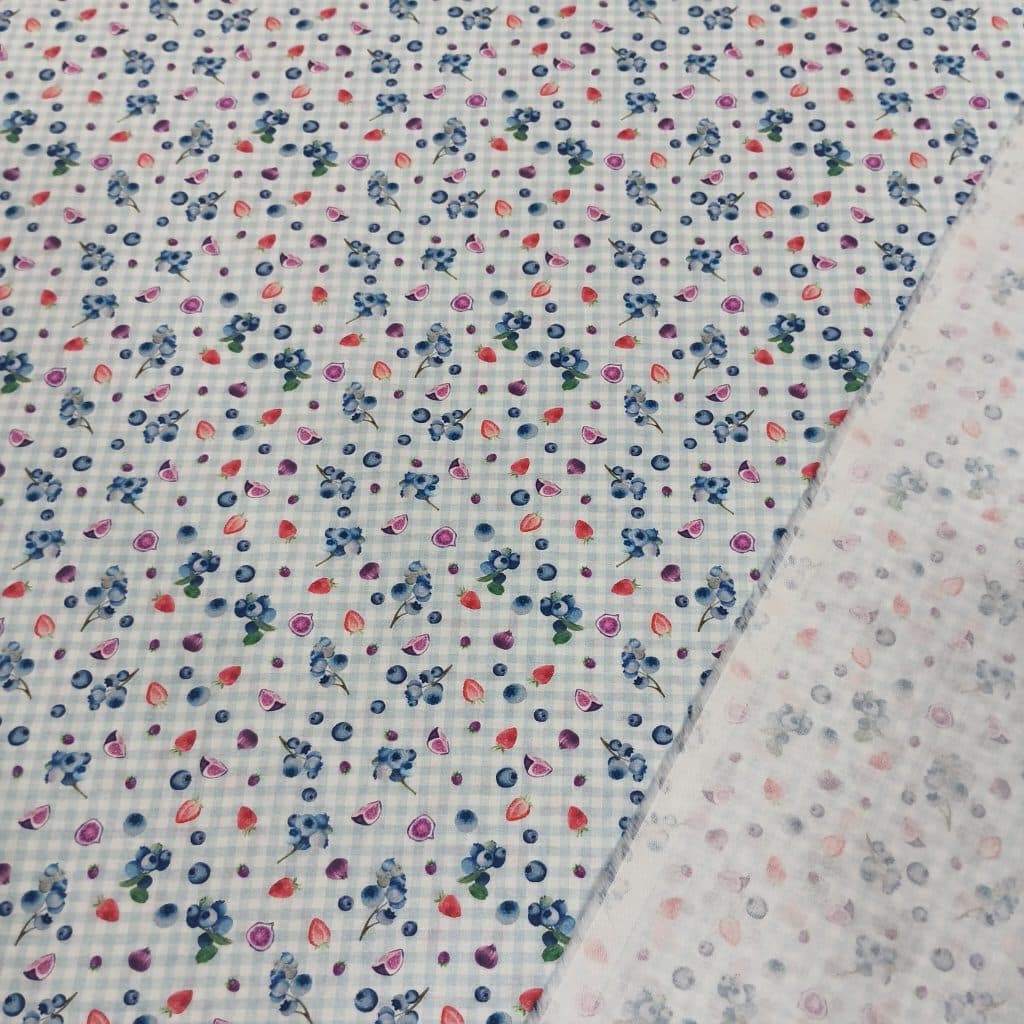 Tela de algodon 100% con estampado de frutas de temporada de verano, como arandanos, fresas, higos. El fondo del tejido es a cuadritos en un vichy muy clarito azul y blanco. Su textura es muy suave.