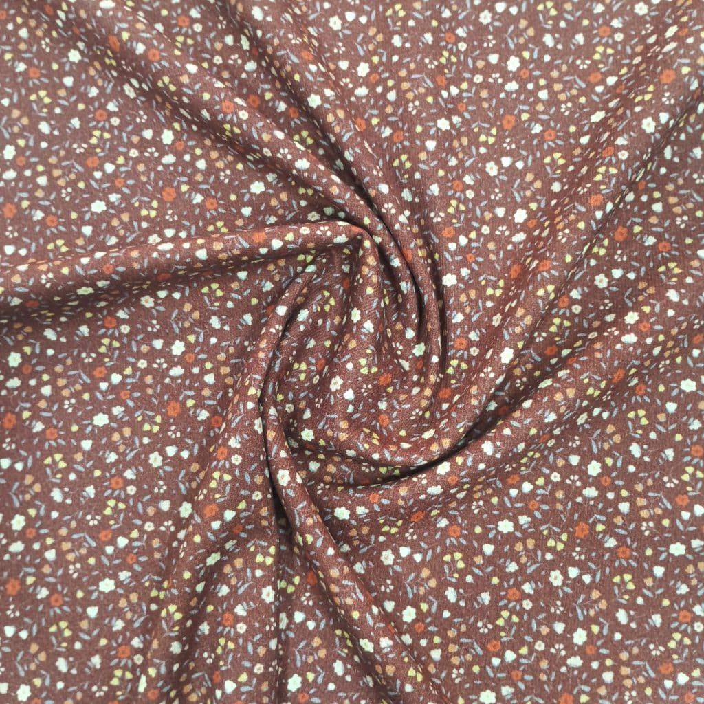 Tela de piqué de algodón 100% con fondo marron presenta en fondo marrón un estampado de florecitas pequeñas en tonos tierra.