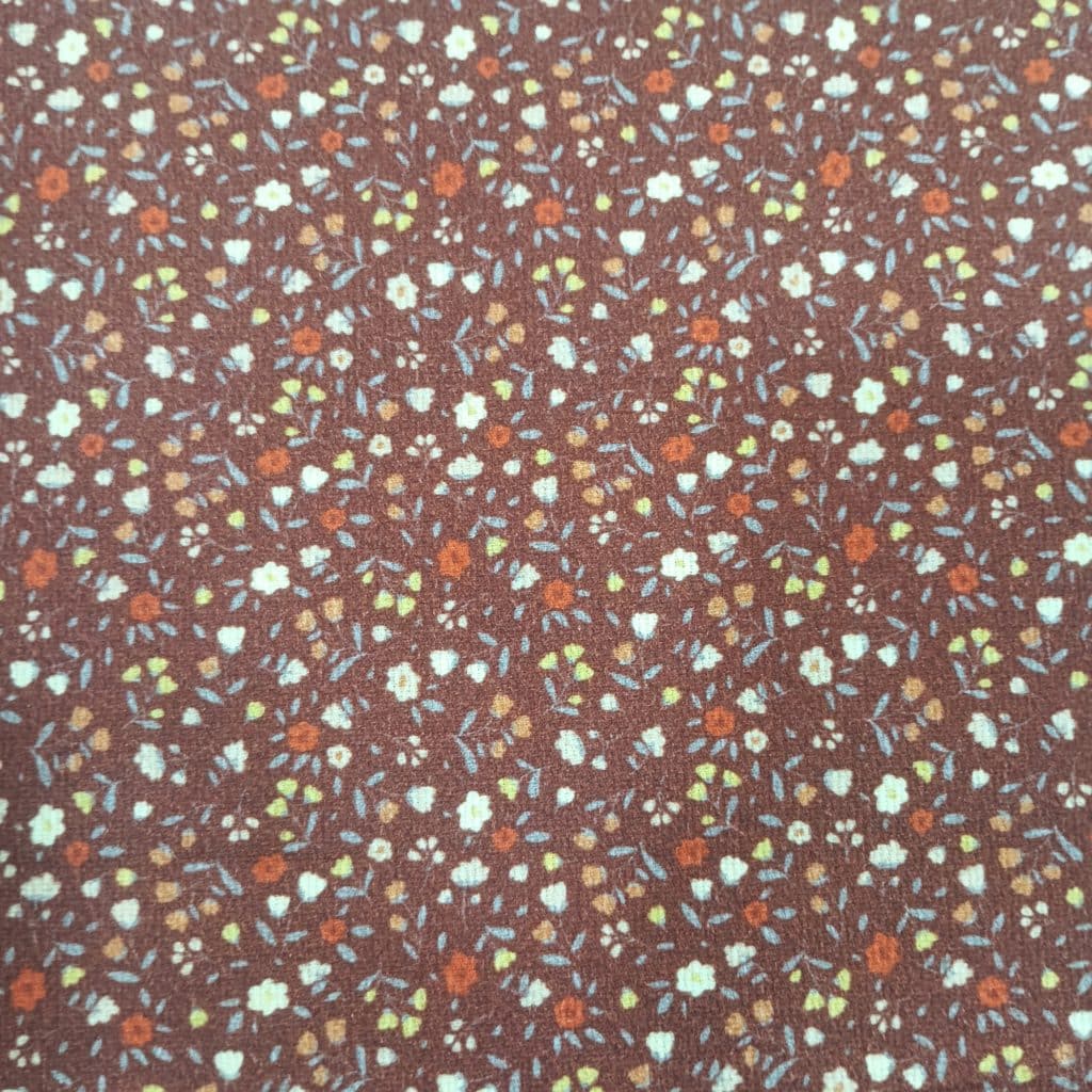 Tela de piqué de algodón 100% con fondo marron presenta en fondo marrón un estampado de florecitas pequeñas en tonos tierra.
