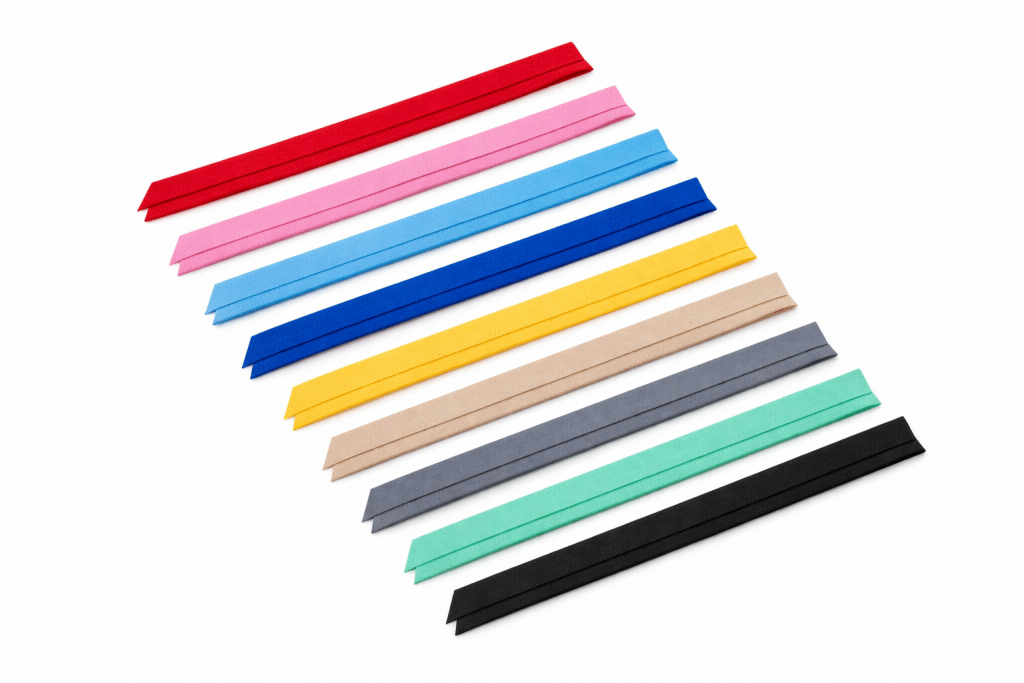 Bieses de tela en varios colores — rojo, rosa, azul claro, azul marino, amarillo, beige, gris, verde menta y negro — dispuestos sobre fondo blanco