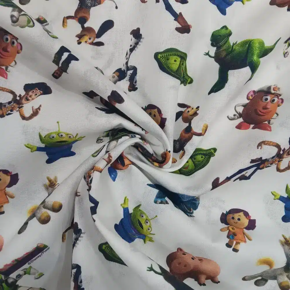 Tela de algodón con licencia Disney Toy Story con personajes como Woody, Buzz Lightyear, Jessie y los marcianitos sobre fondo claro.