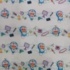 tela-algodon-licencia-doraemon-1 Tela de algodón con estampado de licencia Doraemon, mostrando al personaje azul sonriente junto a elementos amarillos y rojos sobre un fondo blanco.