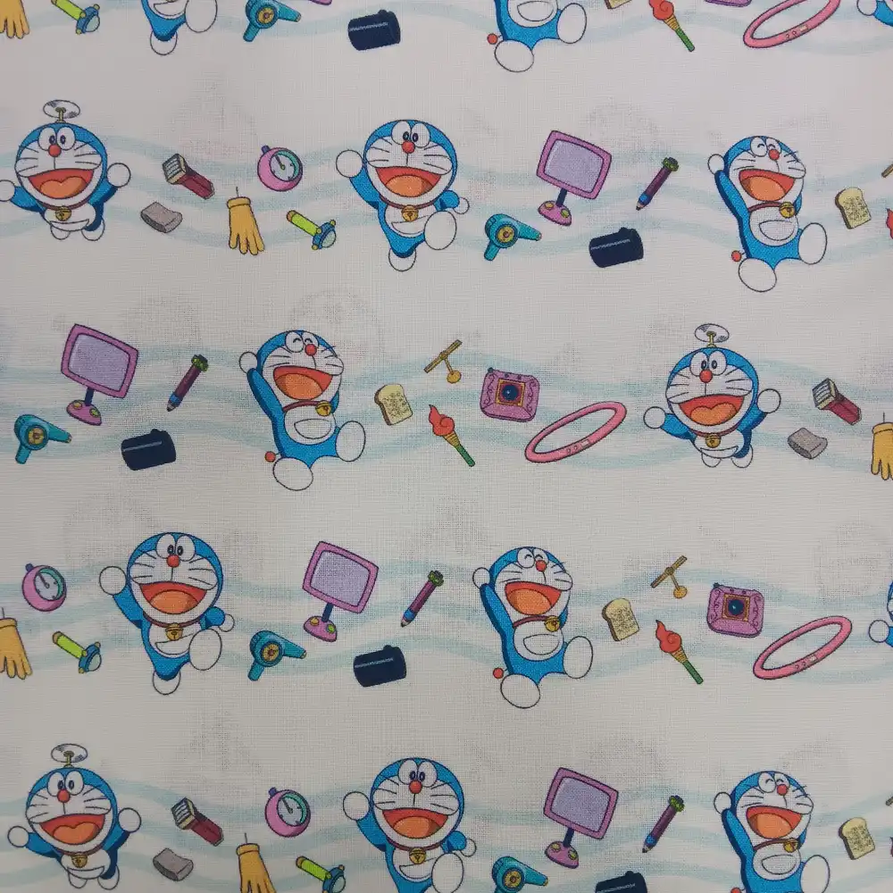 tela-algodon-licencia-doraemon-1 Tela de algodón con estampado de licencia Doraemon, mostrando al personaje azul sonriente junto a elementos amarillos y rojos sobre un fondo blanco.