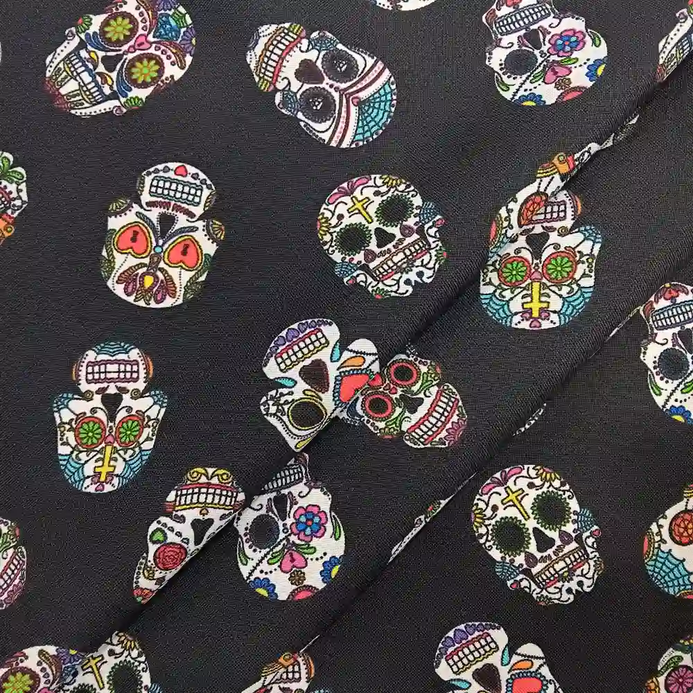 Imagen de una tela de poliéster de fondo negro con un patrón repetido de calaveras mexicanas decoradas con colores vivos como rosa, verde, azul, amarillo y rojo.