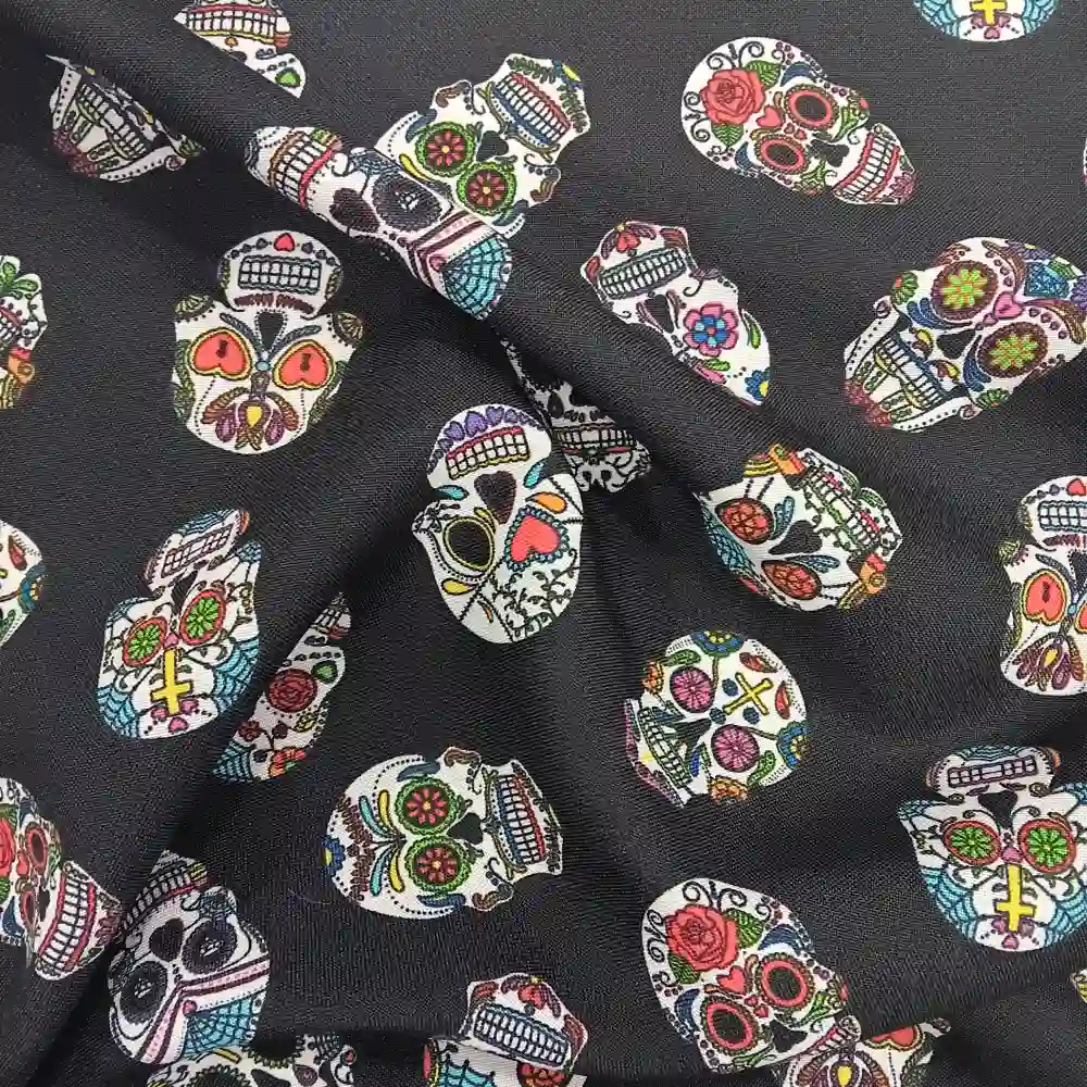 Imagen de una tela de poliéster de fondo negro con un patrón repetido de calaveras mexicanas decoradas con colores vivos como rosa, verde, azul, amarillo y rojo.