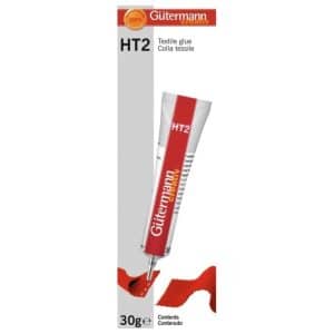 Tubo de cola textil Gütermann HT2 de 30 g sobre fondo blanco. El envase muestra el diseño rojo y blanco con la marca Gütermann creativ y la inscripción “Textile glue – Colla tessile”. Se observa el adhesivo aplicado sobre una tela roja.