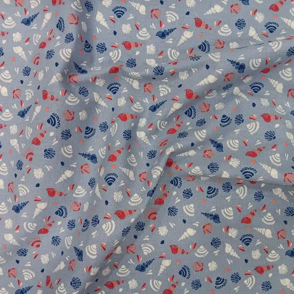 Tela de algodón estampada con caracolas marinas y conchas en tonos azul, coral y blanco sobre fondo azul claro.
