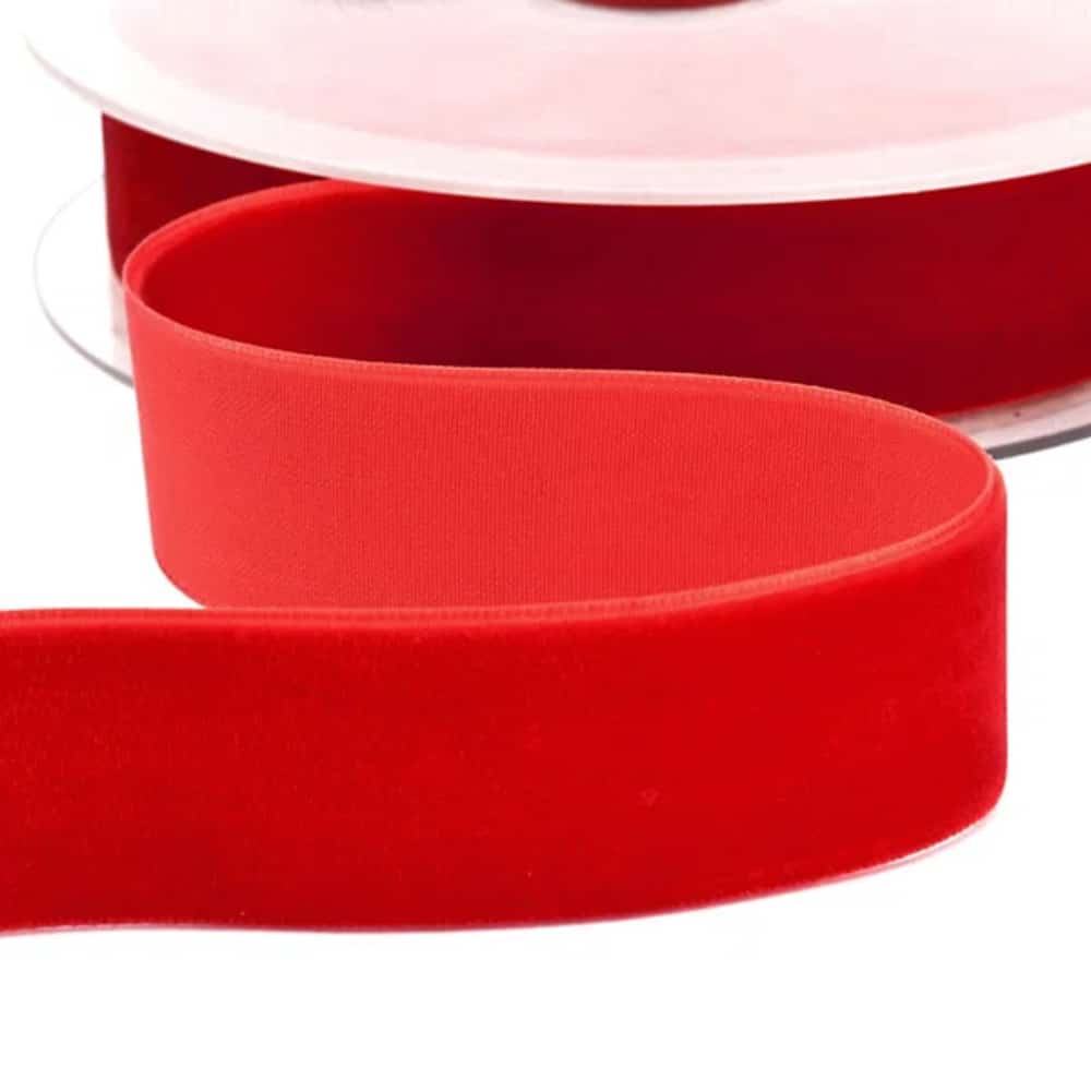 Cinta de terciopelo rojo intenso enrollada en carrete transparente, con un tramo extendido mostrando su textura suave y aterciopelada