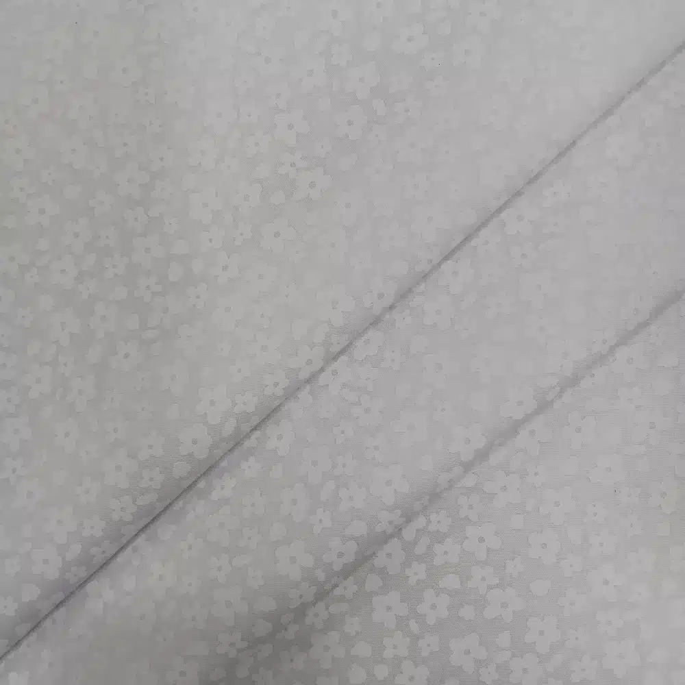 Tela de algodón blanca con estampado floral blanco de pequeñas flores distribuidas sobre fondo blanco.