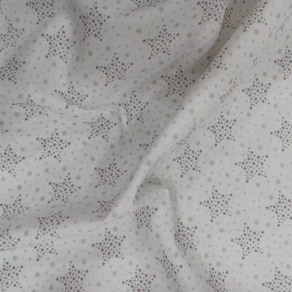 Tela de algodón blanca con estrellas punteadas grises y pequeñas estrellas distribuidas sobre fondo blanco.