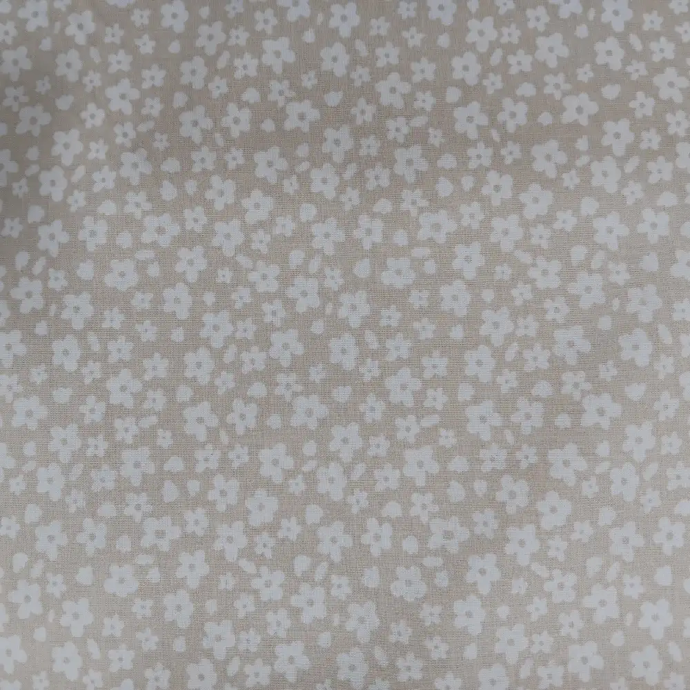 Tela de algodón estampada beige con pequeñas flores blancas distribuidas sobre fondo beige claro.