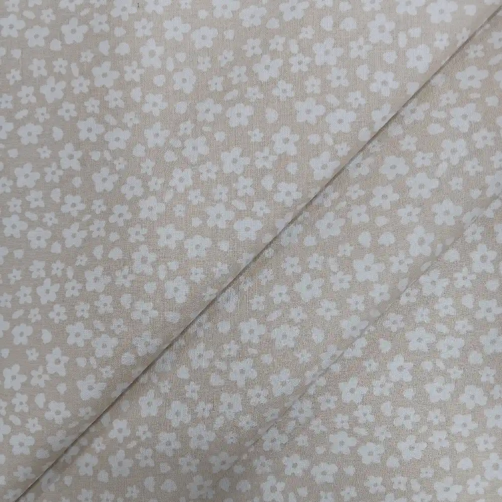 Tela de algodón estampada beige con pequeñas flores blancas distribuidas sobre fondo beige claro.