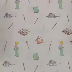 Tela de algodón estampado El Principito sobre fondo claro, con personajes, zorro, libros, lápices y pequeños motivos distribuidos por el tejido.