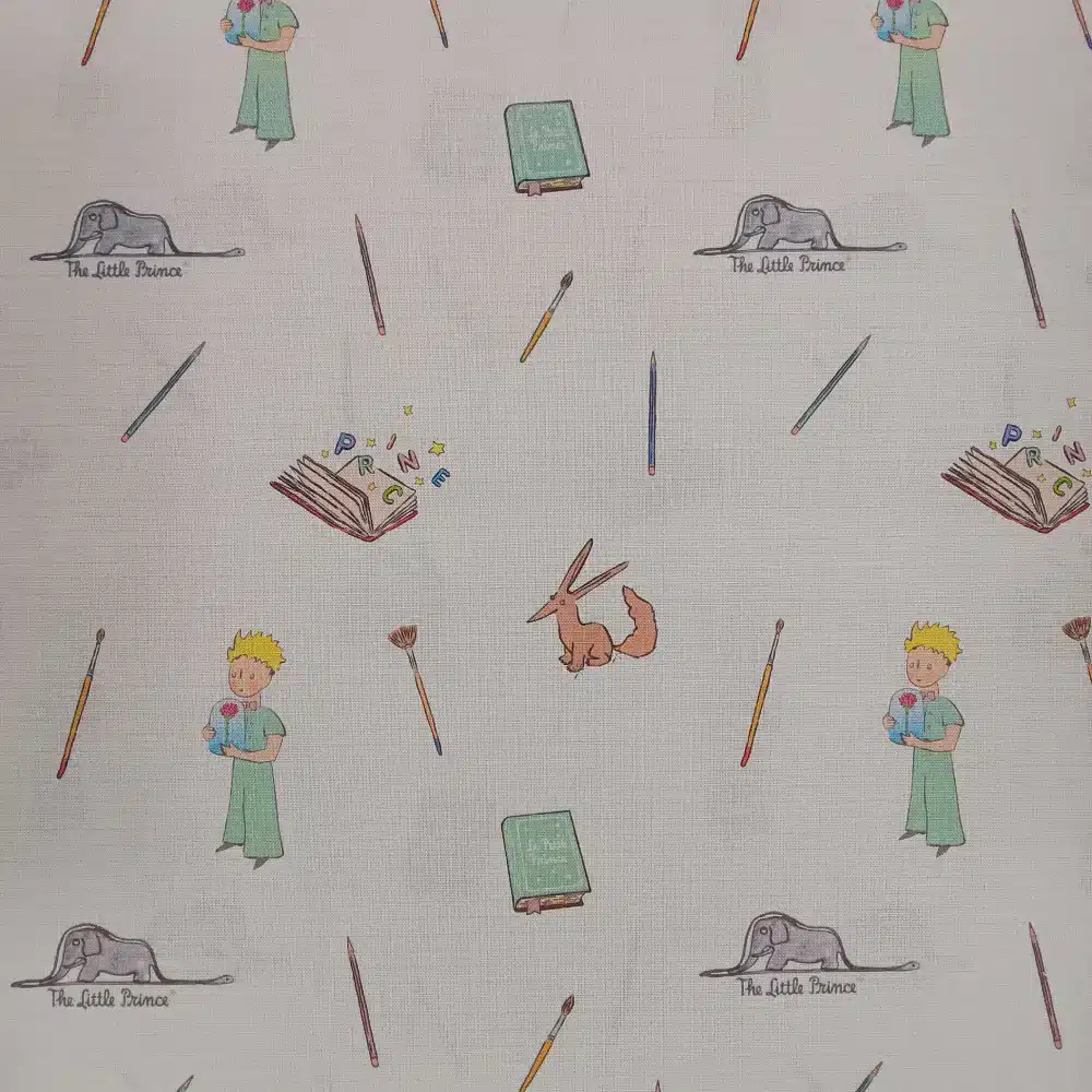 Tela de algodón estampado El Principito sobre fondo claro, con personajes, zorro, libros, lápices y pequeños motivos distribuidos por el tejido.