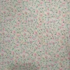 Tela de algodón blanca estampada con numerosas flores pequeñas en tonos rosas, hojas verdes y diminutos detalles amarillos, distribuidos por toda la superficie.