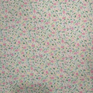Tela de algodón blanca estampada con numerosas flores pequeñas en tonos rosas, hojas verdes y diminutos detalles amarillos, distribuidos por toda la superficie.