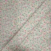 Tela de algodón blanca estampada con numerosas flores pequeñas en tonos rosas, hojas verdes y diminutos detalles amarillos, distribuidos por toda la superficie.