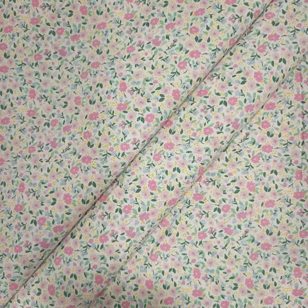 Tela de algodón blanca estampada con numerosas flores pequeñas en tonos rosas, hojas verdes y diminutos detalles amarillos, distribuidos por toda la superficie.