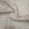 Tela de algodón blanca estampada con numerosas flores pequeñas en tonos rosas, hojas verdes y diminutos detalles amarillos, distribuidos por toda la superficie.