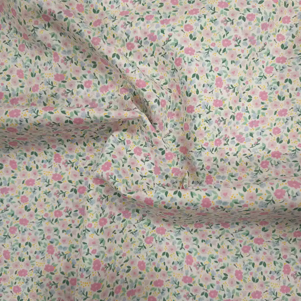 Tela de algodón blanca estampada con numerosas flores pequeñas en tonos rosas, hojas verdes y diminutos detalles amarillos, distribuidos por toda la superficie.