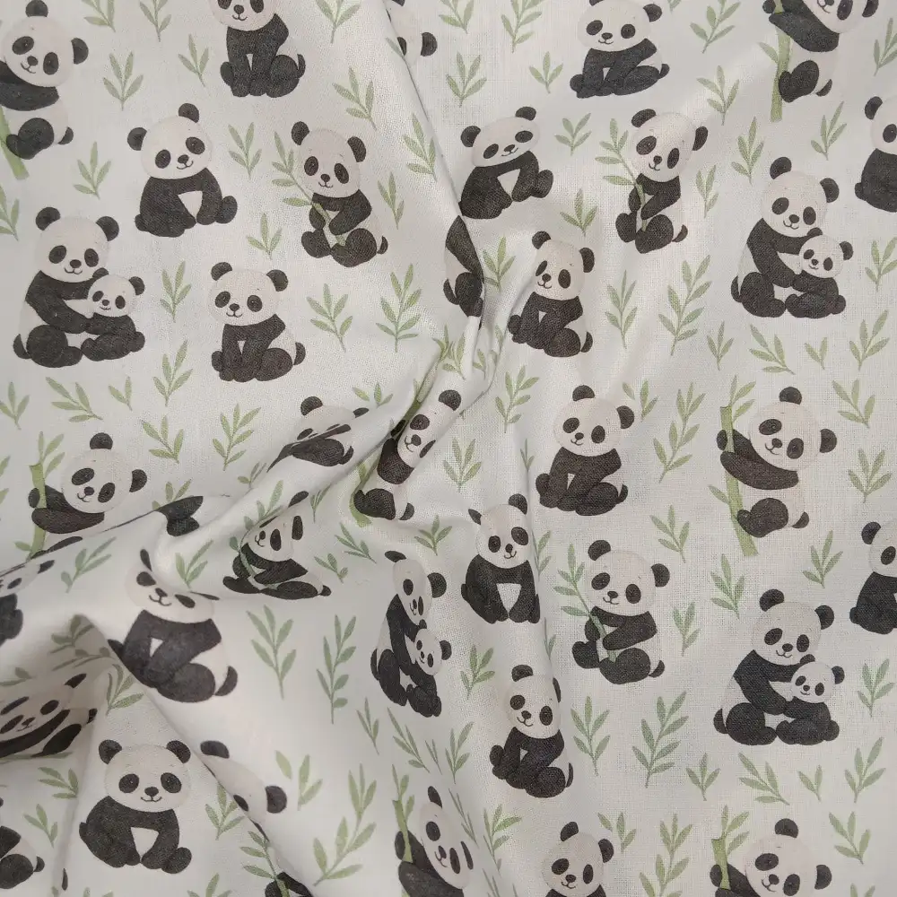 Tela de algodón estampada con osos panda sobre fondo claro, con pandas en diferentes posturas, pequeñas ramas verdes y motivos de bambú.