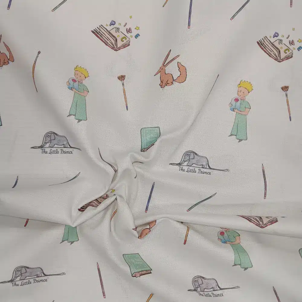 Tela de algodón estampado El Principito sobre fondo claro, con personajes, zorro, libros, lápices y pequeños motivos distribuidos por el tejido.