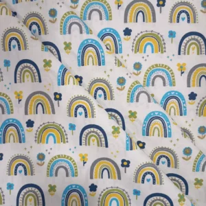 Tela de algodón infantil estampada con arcoíris azules, amarillos, verdes y grises, acompañados de pequeñas flores y corazones sobre fondo claro.