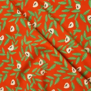 Tela de algodón naranja con flores beige de centros oscuros y ramas de hojas verdes alargadas, distribuidas sobre un fondo naranja intenso.