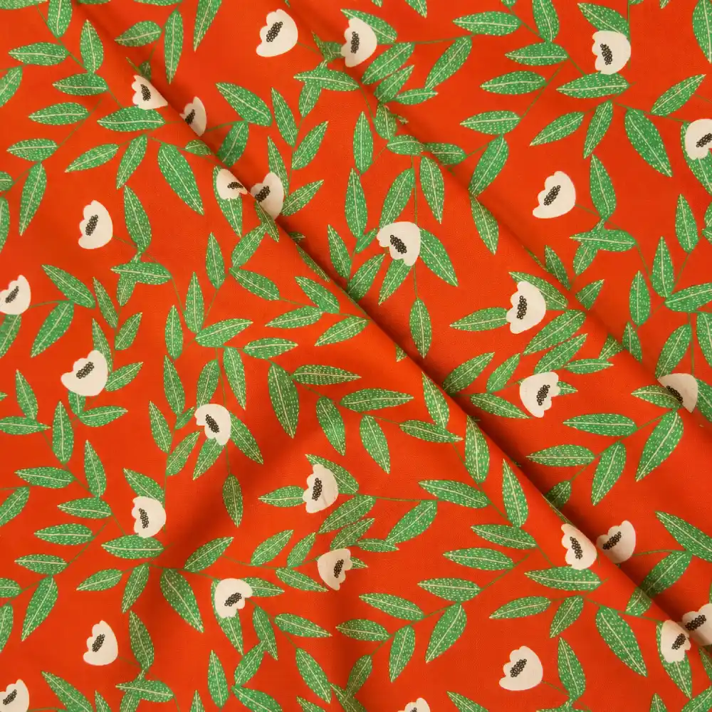 Tela de algodón naranja con flores beige de centros oscuros y ramas de hojas verdes alargadas, distribuidas sobre un fondo naranja intenso.