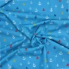 Tela de algodón azul con pequeñas anclas estampadas de diferentes tamaños en blanco, rojo, amarillo y azul marino, distribuidas por toda la superficie.