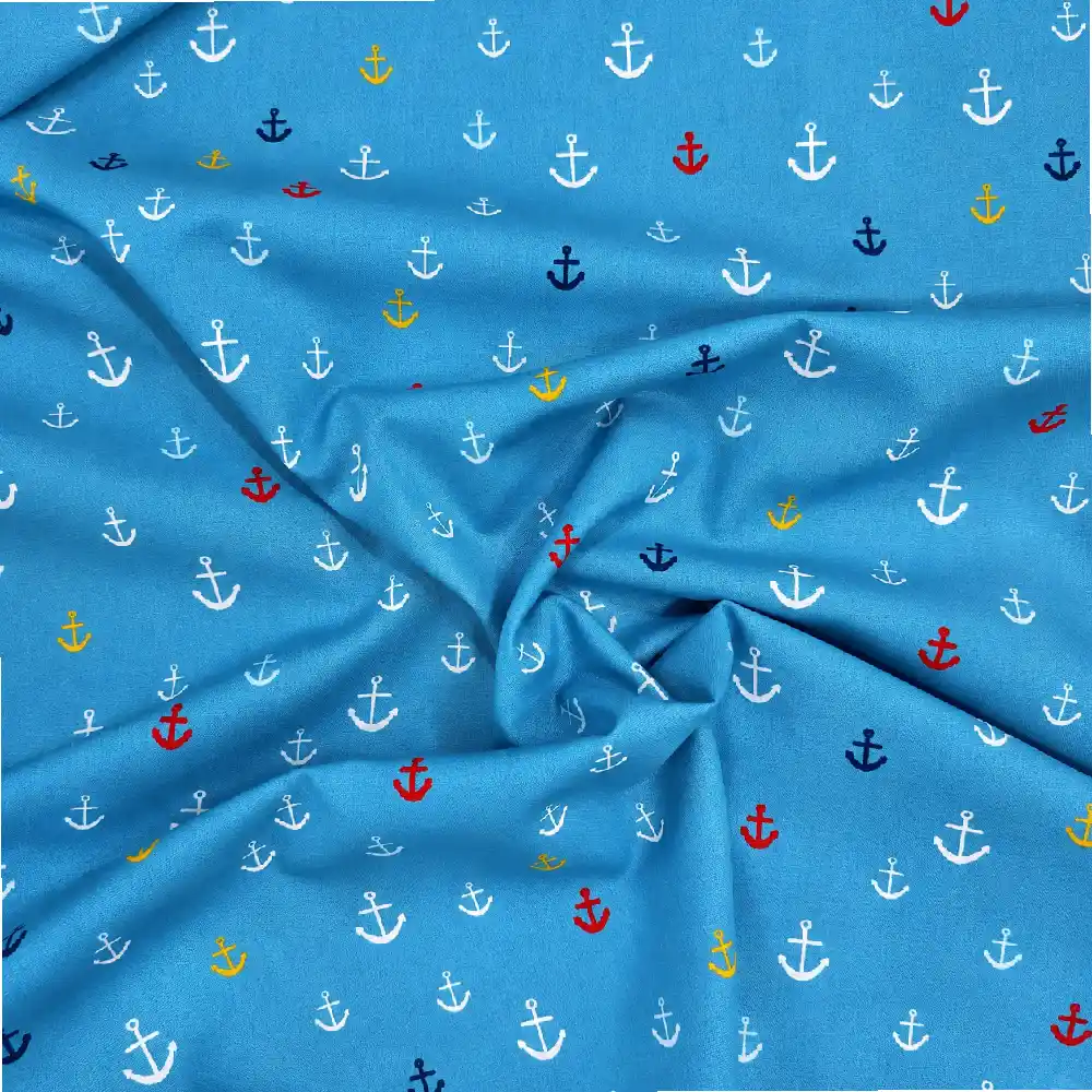 Tela de algodón azul con pequeñas anclas estampadas de diferentes tamaños en blanco, rojo, amarillo y azul marino, distribuidas por toda la superficie.