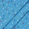 Tela de algodón azul con pequeñas anclas estampadas de diferentes tamaños en blanco, rojo, amarillo y azul marino, distribuidas por toda la superficie.