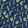 Tela de algodón azul oscuro con estampado de ramas y hojas de eucalipto en diferentes tonos verdes, amarillos suaves y crema, distribuidas sobre el fondo.