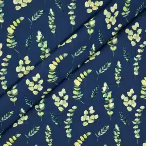 Tela de algodón azul oscuro con estampado de ramas y hojas de eucalipto en diferentes tonos verdes, amarillos suaves y crema, distribuidas sobre el fondo.
