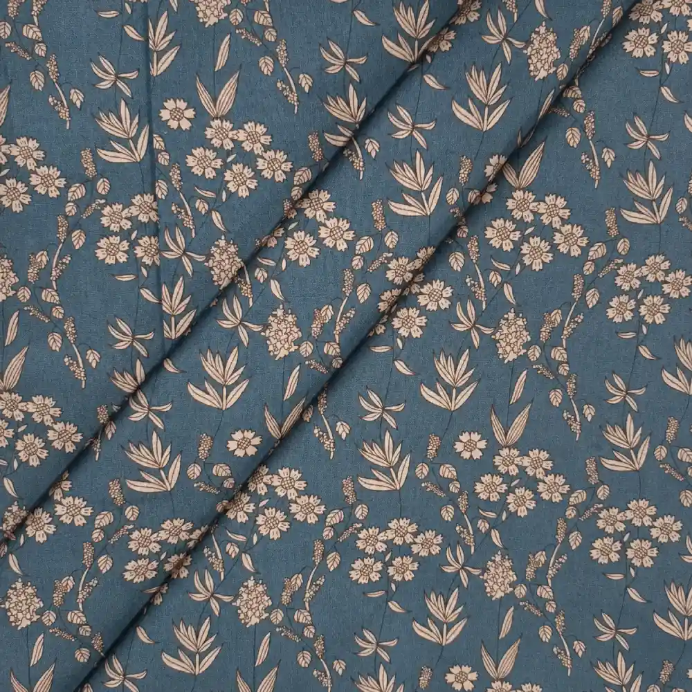 Tela de algodón azul petróleo con flores beige y estampado botánico, presentada con varios pliegues diagonales.