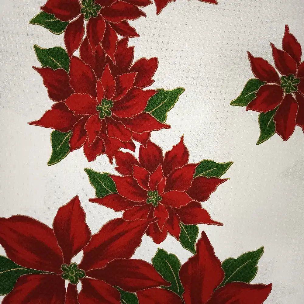 Tela de mantelería navideña blanca con grandes flores de Pascua rojas y burdeos, hojas verdes y finos contornos dorados, sobre fondo blanco con textura.