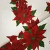 Tela de mantelería navideña blanca con grandes flores de Pascua rojas y burdeos, hojas verdes y finos contornos dorados, sobre fondo blanco con textura.